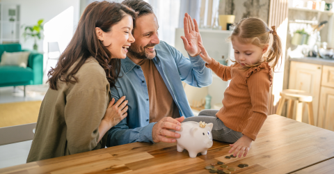 Een kind zit op tafel en telt met haar ouders het muntgeld uit haar spaarvarken